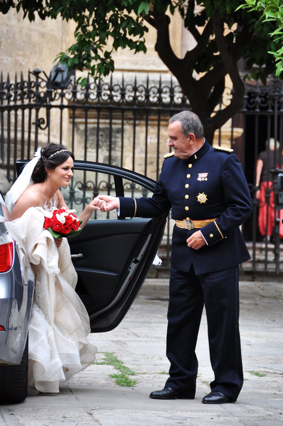 A bride gracefully escorted out of the wedding car by her father.